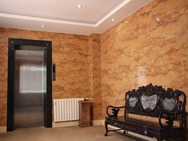 Un vestíbulo con pared de mármol, un ascensor, un radiador y un banco.