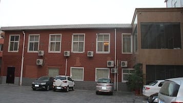Un estacionamiento con varios autos, un edificio de ladrillo rojo con múltiples ventanas y unidades de aire acondicionado, y un edificio moderno con grandes ventanales.