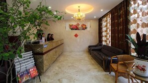 A reception area with a marble counter, a sofa, a wicker chair, and a chandelier. - Shuyang Sanhe Hotel (Puyang)