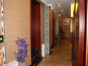 Un couloir d’hôtel avec un mur orné de motifs, un vase décoratif et un escalier au loin.
