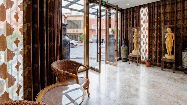 A hotel lobby with a glass door entrance, wicker chairs, and statues on pedestals. - Shuyang Sanhe Hotel (Puyang)