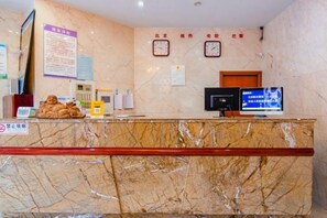 Un comptoir d’accueil d’hôtel avec un revêtement en marbre, un téléviseur, des horloges et un panneau indiquant qu’il est interdit de fumer.