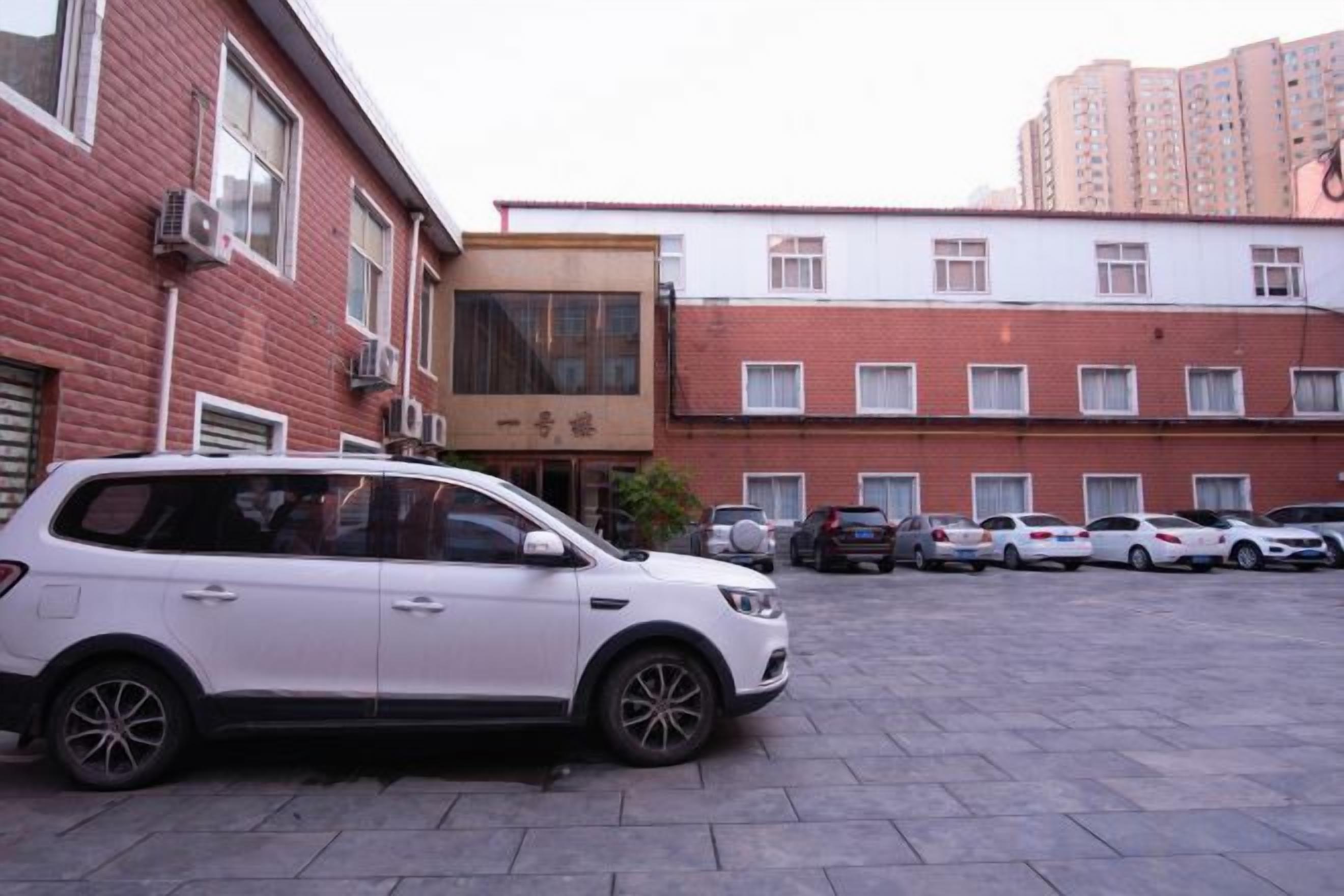 A parking area with multiple cars, a white SUV, and a building with a red brick facade and a sign.