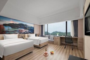 Habitación de hotel con dos camas, un escritorio, una silla, un ventanal con vistas y un cuadro en la pared.