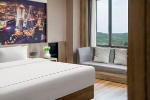 Una habitación de hotel moderna con una cama grande, un sofá, un televisor y vistas a un paisaje urbano.