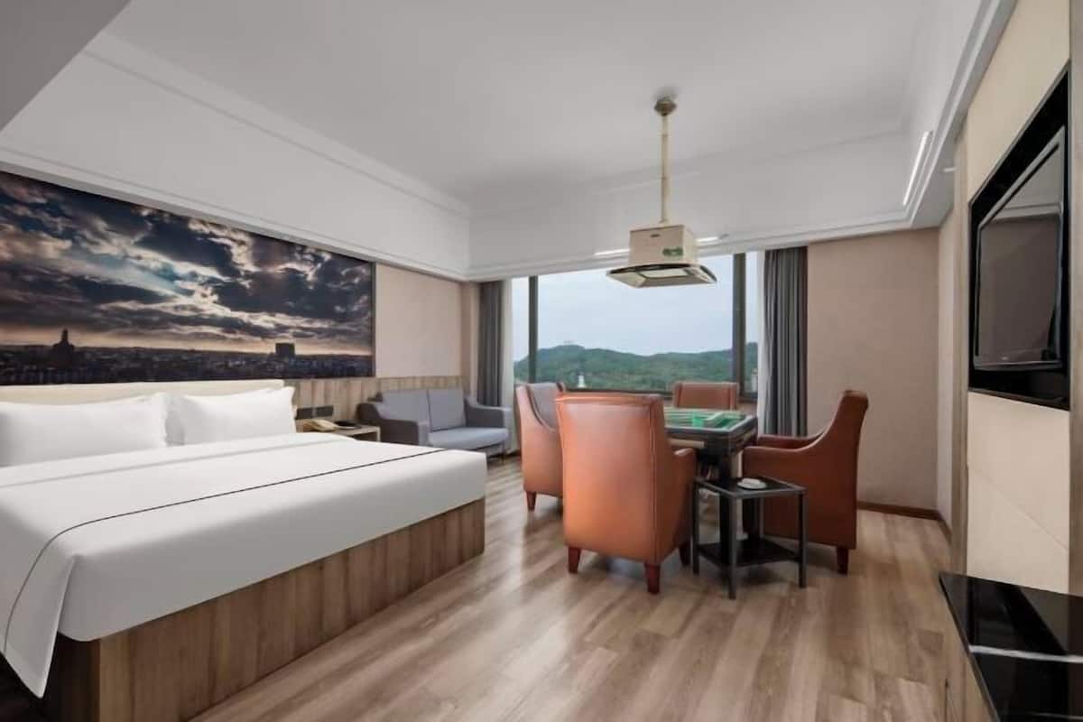 Une chambre d’hôtel comprenant un lit, une table à manger avec des chaises, un téléviseur et une grande fenêtre donnant sur le paysage urbain.