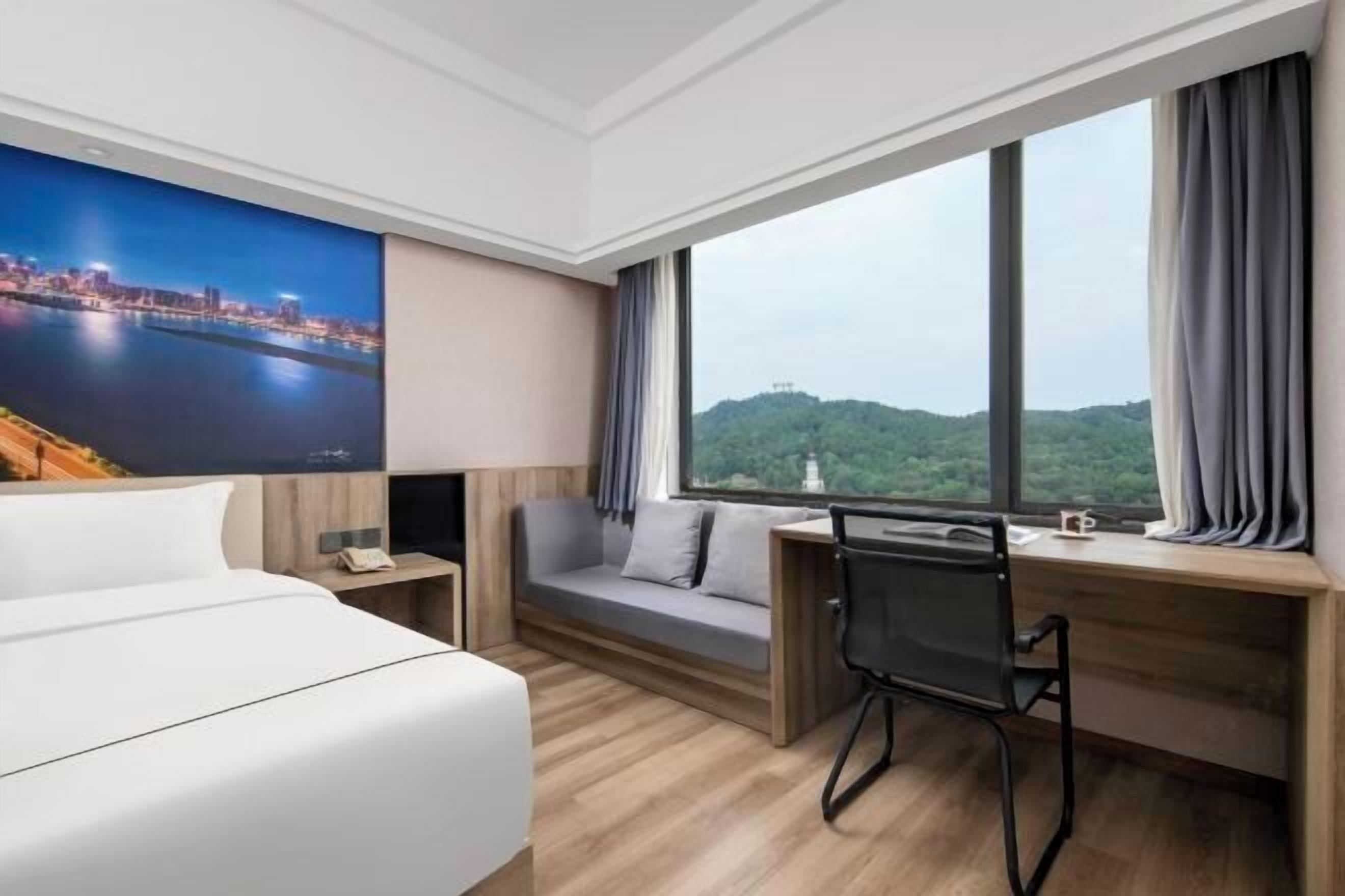 A hotel room with a bed, a desk, a chair, a TV, and a large window with curtains.