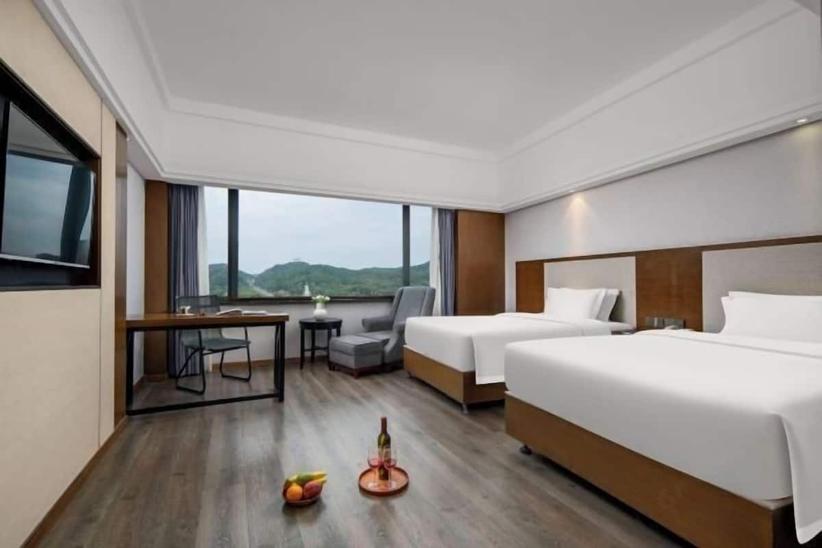 Une chambre d’hôtel avec deux lits, un bureau, une chaise, une petite table et une vue sur l’extérieur.