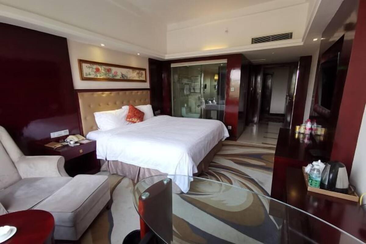 Une chambre d’hôtel avec un grand lit, un canapé, une table basse en verre et une salle de bain visible à travers une porte en verre.