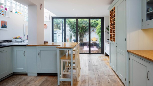A modern kitchen with light blue cabinets, a wooden countertop, and a large sliding glass door leading to an outdoor patio. - Thames-side Retreat, by Veeve (London)