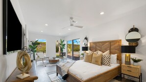A modern bedroom with a large bed, a ceiling fan, a wooden headboard, and a view of the outdoors. - Newly renovated 4-bedroom house with pool and two main suites in Palm Springs.  (Palm Springs)