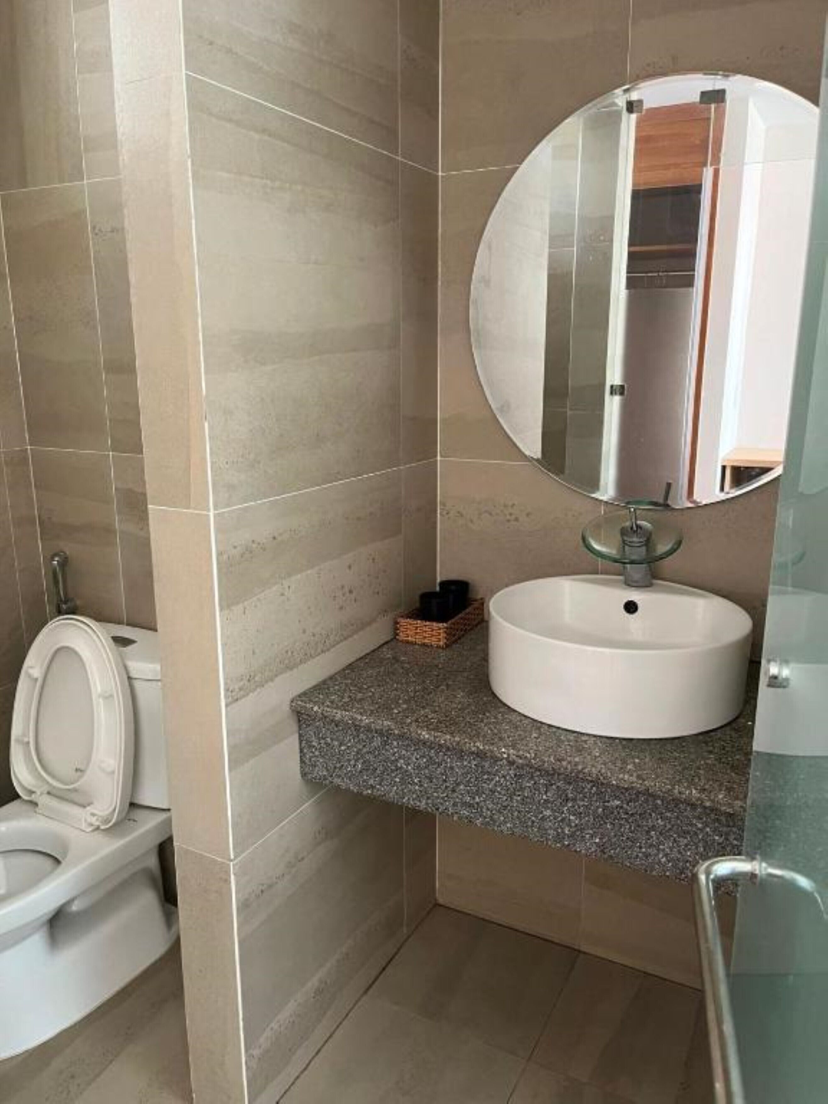 A bathroom with a white sink, a round mirror, and a toilet.