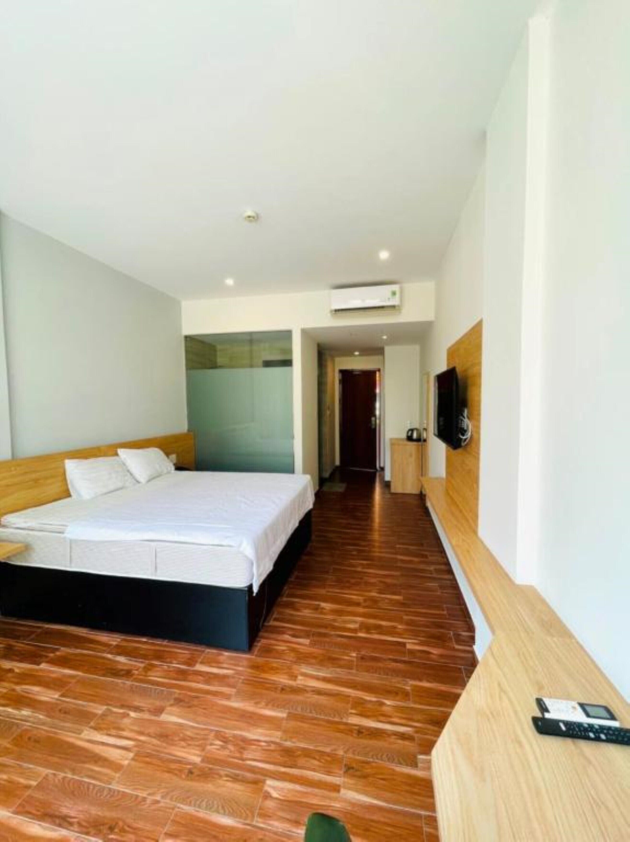 Quarto de hotel moderno com piso de madeira, uma cama grande, TV na parede e uma pequena mesa com telefone.