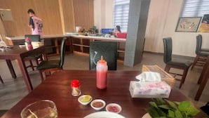 Uma mesa de jantar com uma tigela de sopa, uma garrafa de molho, temperos e ervas frescas.