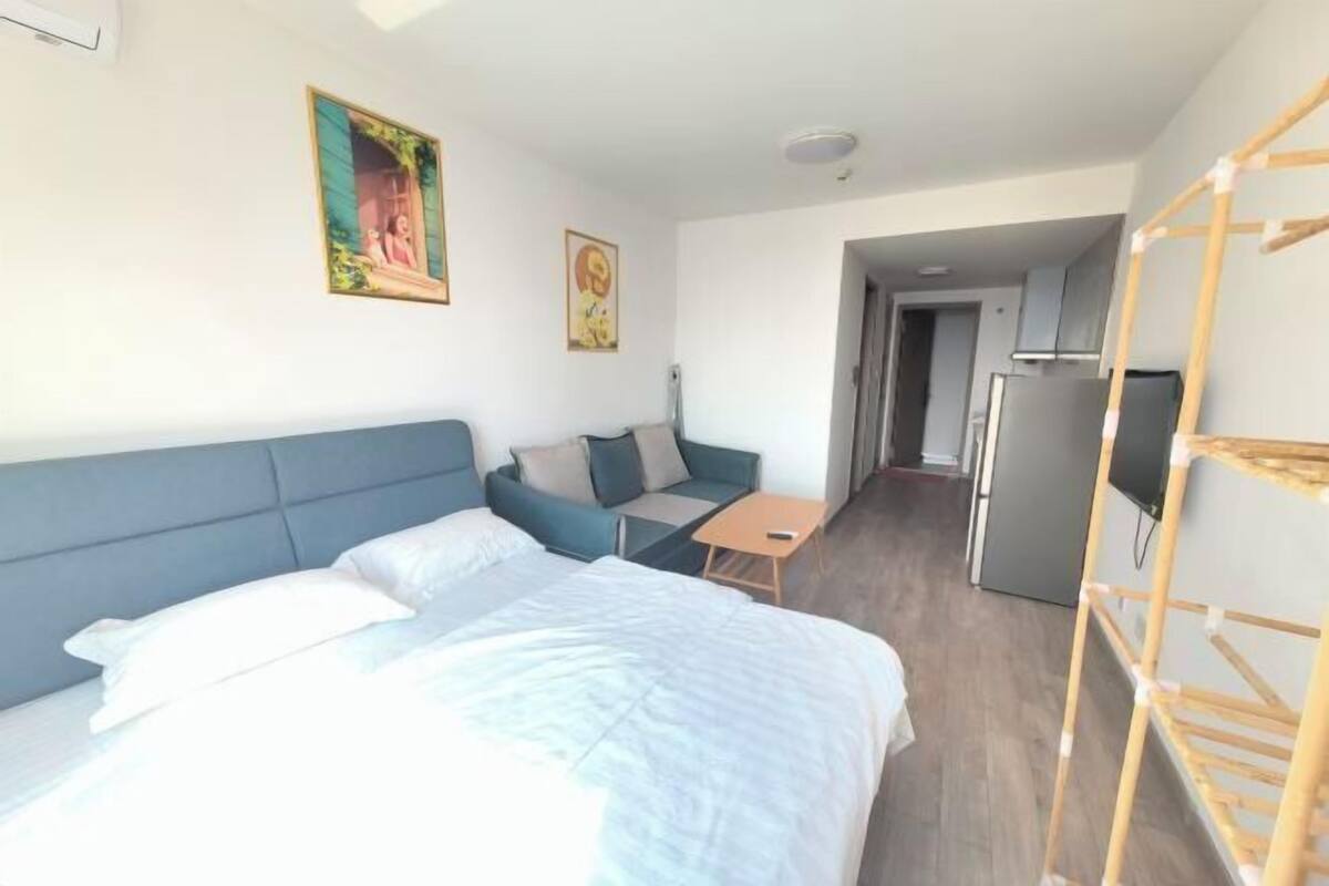 Una habitación de hotel con cama, sofá, una mesita, televisor y zona de cocina.