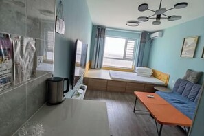 A compact hotel room with a bed, a small table, a sofa, a TV, and a window with curtains.