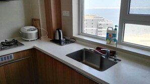 A modern kitchen with a gas stove, a coffee maker, a sink, and a window with a view of buildings. - Yingkou Vanke Letu Seaview Apartment (Yingkou)