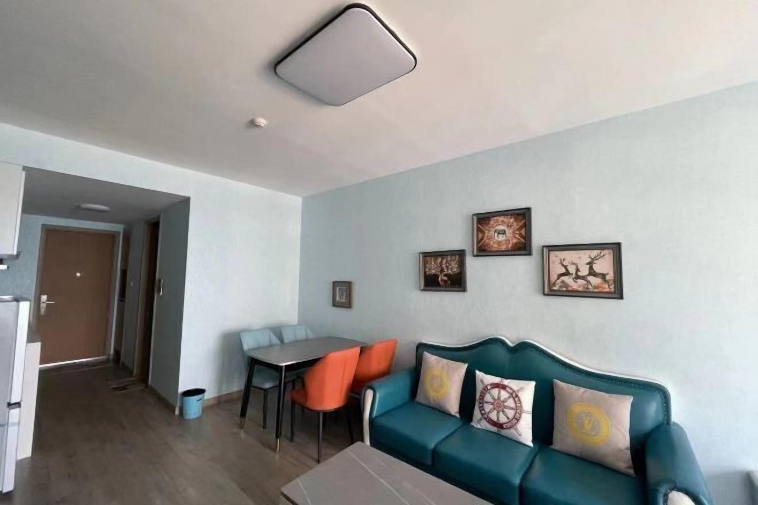 Una sala de estar con un sofá azul verdoso, sillas anaranjadas, una mesa de comedor y una zona de cocina.