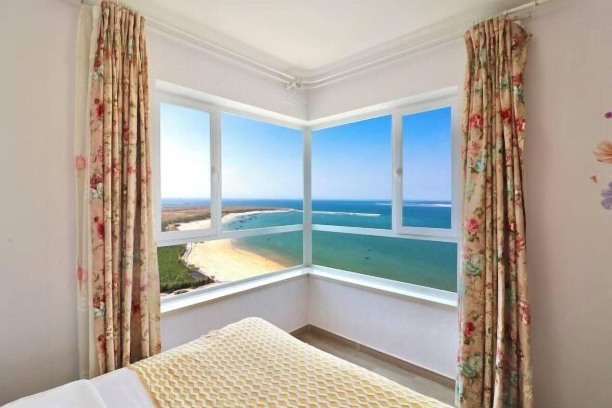 Habitación de esquina con cama, cortinas florales y vista al mar.