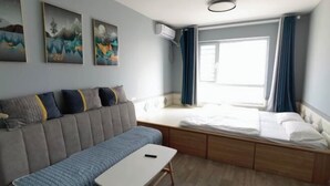 A modern room with a sofa, a small table, a bed with a wooden frame, and a window with curtains. - Yingkou Vanke Letu Seaview Apartment (Yingkou)
