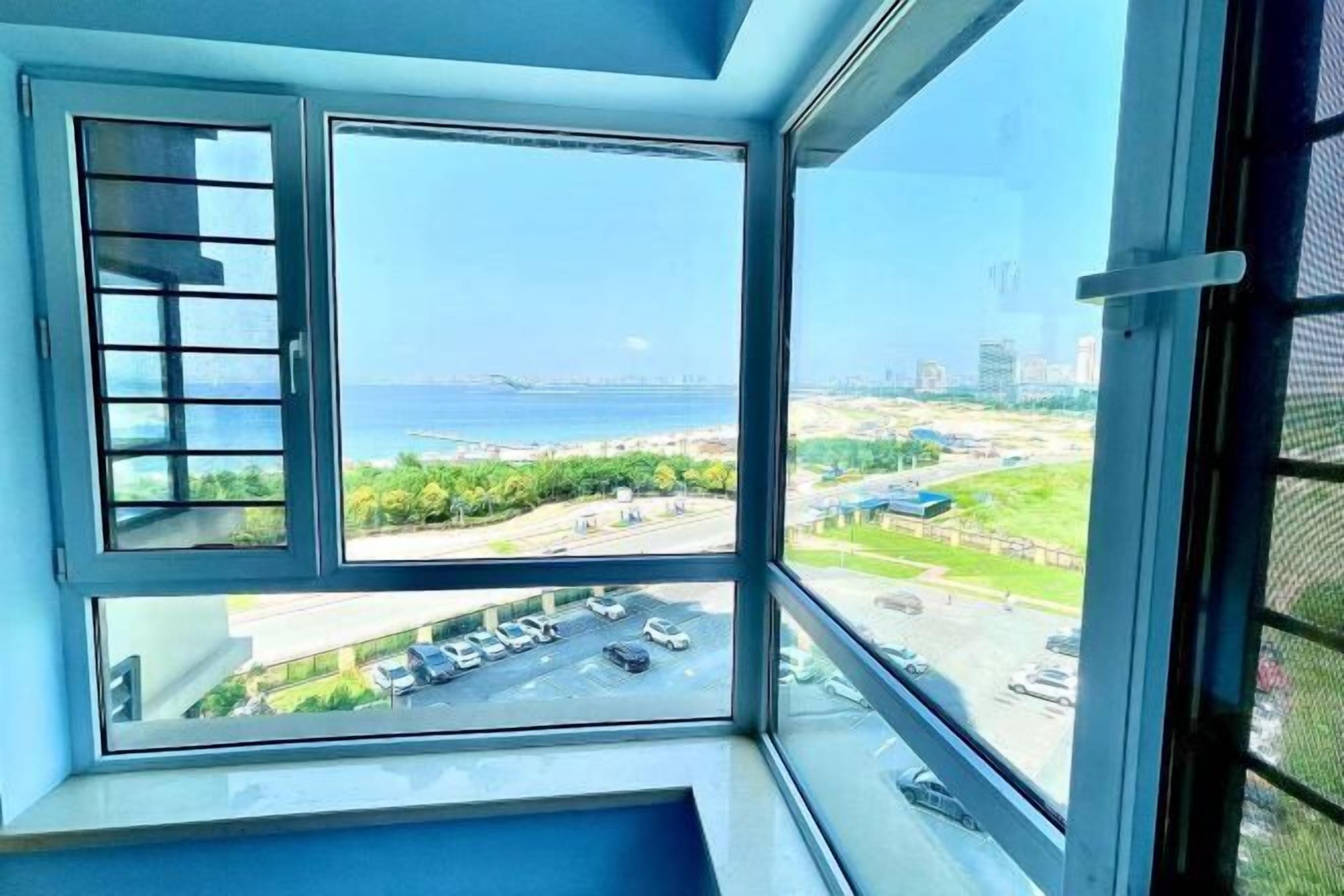 A room with a large window offering a view of a parking lot and a beach.