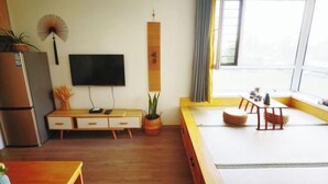 A modern living room with a flat-screen TV, wooden furniture, a potted plant, and a large window with curtains. - Yingkou Vanke Letu Seaview Apartment (Yingkou)