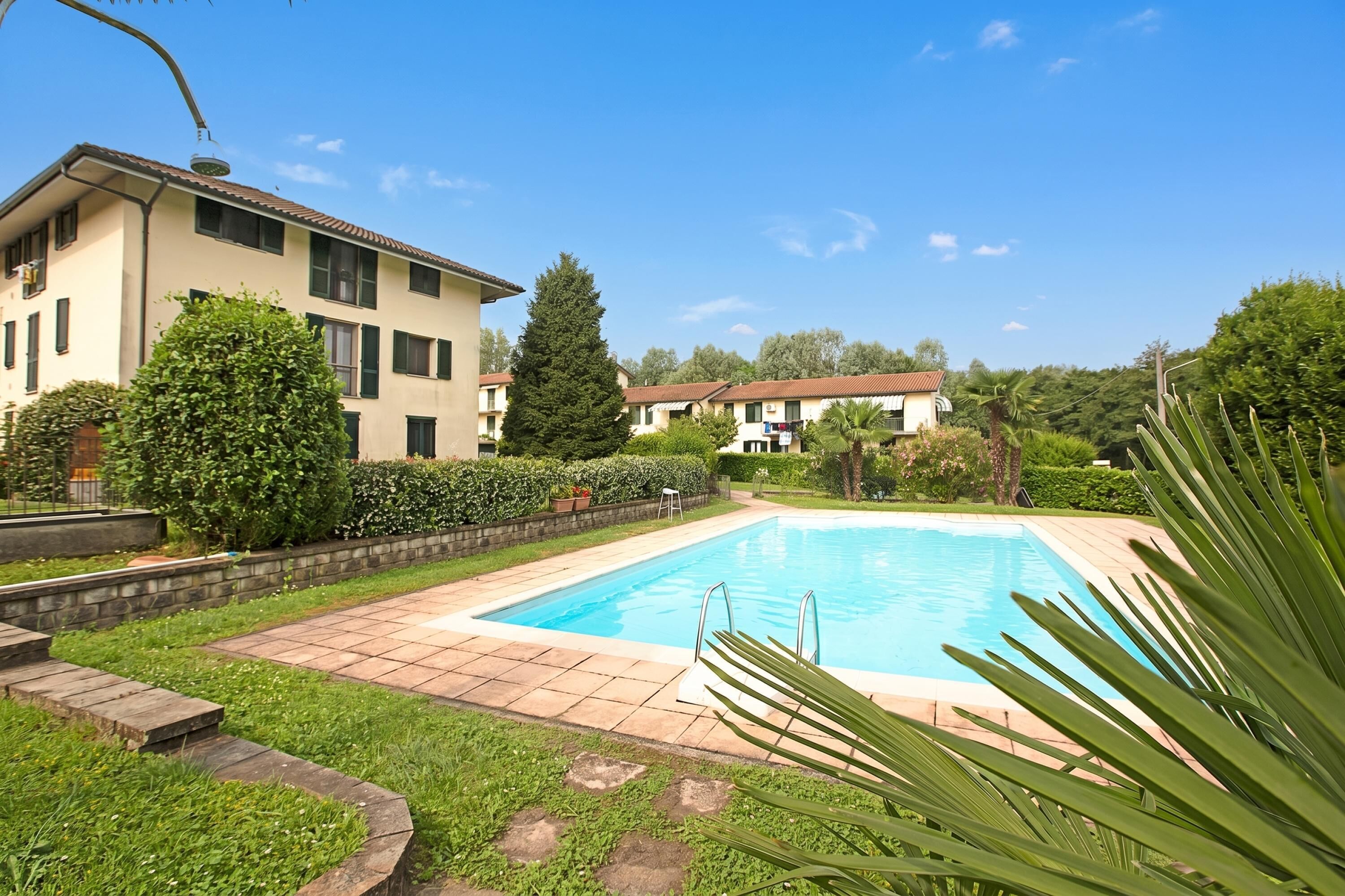 A swimming pool surrounded by a garden with a building in the background.