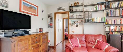 Una sala de estar con un sofá de cuero rojo, un mueble de madera, televisor de pantalla plana, estantería y una puerta que da a otra habitación.