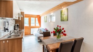 A modern kitchen with wooden cabinets, a built-in oven, and a dining area with a table and chairs. - Apartment in Sankt Gallenkirch Near Ski Slopes (Sankt Gallenkirch)