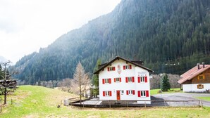 A two-story building with a red and white facade, located in a mountainous area with a forested backdrop. - Apartment in Sankt Gallenkirch Near Ski Slopes (Sankt Gallenkirch)