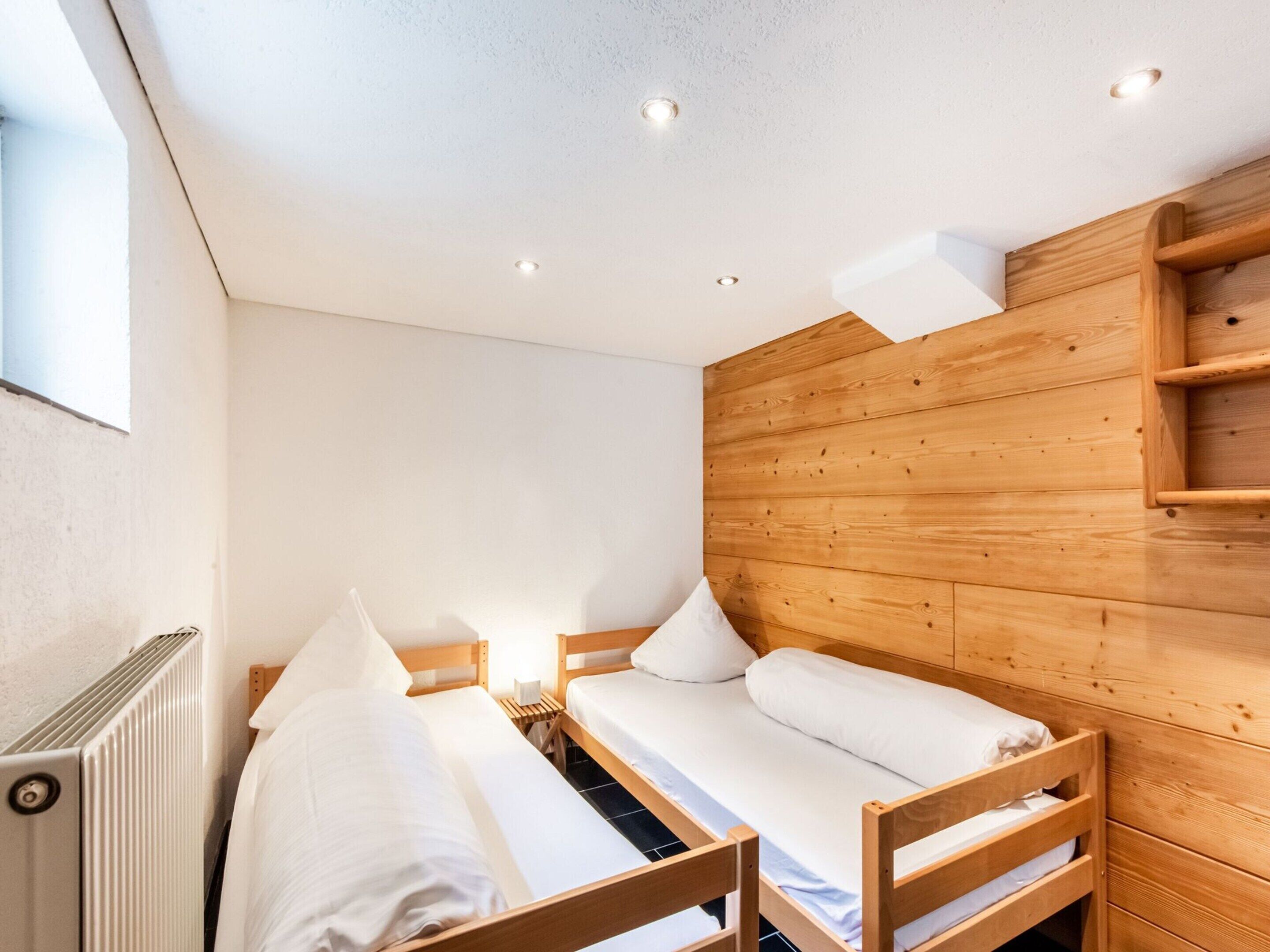 A small, cozy room with two wooden bunk beds, a wooden headboard, and a radiator.