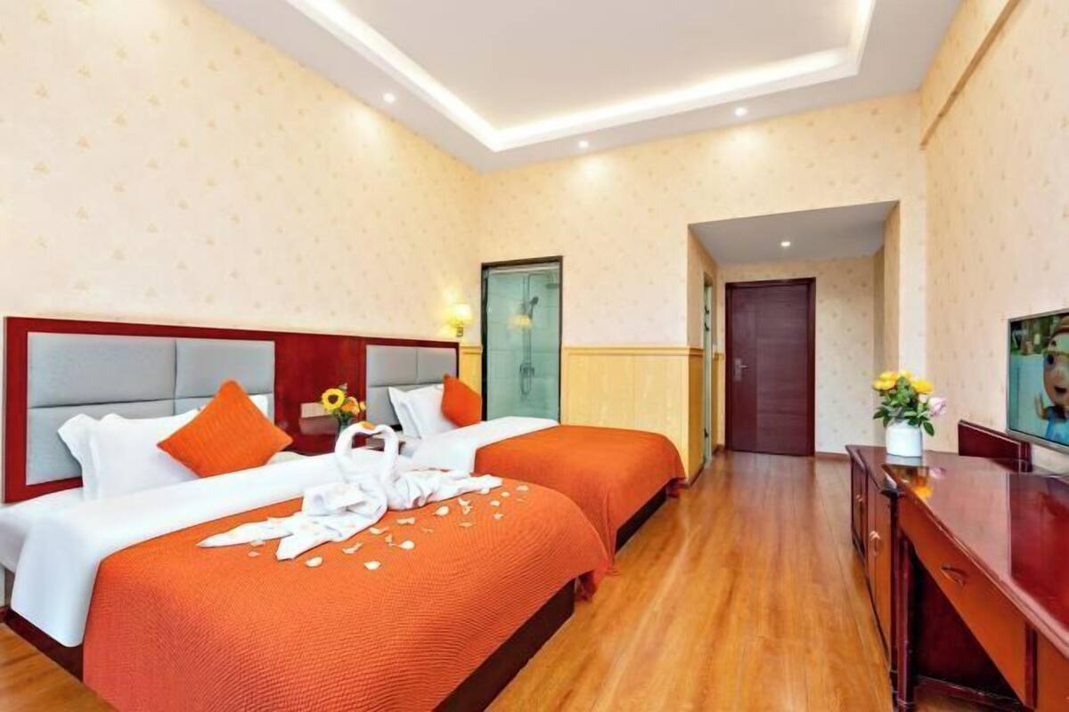 A hotel room with two beds, a wooden floor, a TV, and a desk.