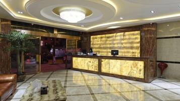 A hotel lobby with a reception desk, seating area, and a chandelier.
