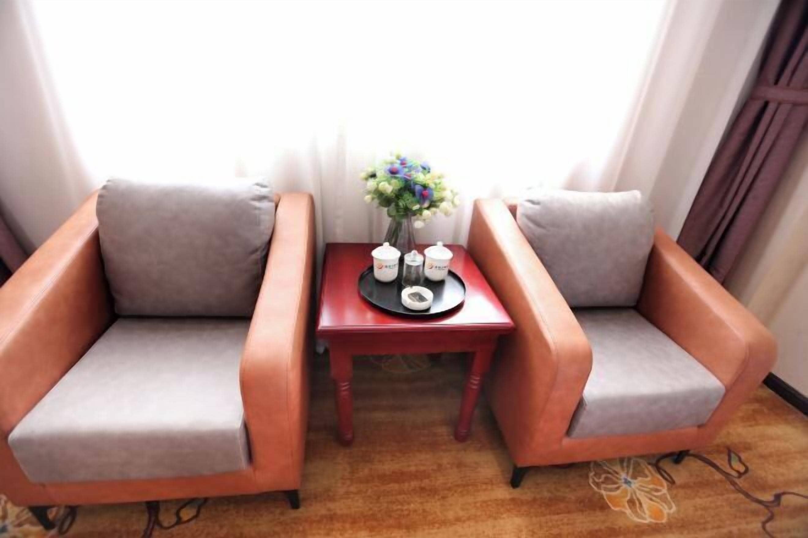 Een kamer met twee fauteuils, een bijzettafeltje met een bloevas en een raam met gordijnen.