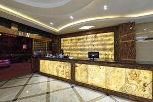 Zona de recepción de un hotel con un mostrador de mármol, un monitor de pantalla plana y una sala de estar con alfombra roja.