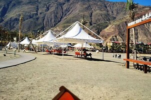 Una playa con carpas blancas y sillas rojas, frente a un paisaje montañoso.