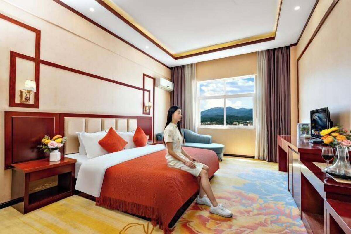A hotel room with a large bed, a desk with a TV, and a view of mountains through the window.