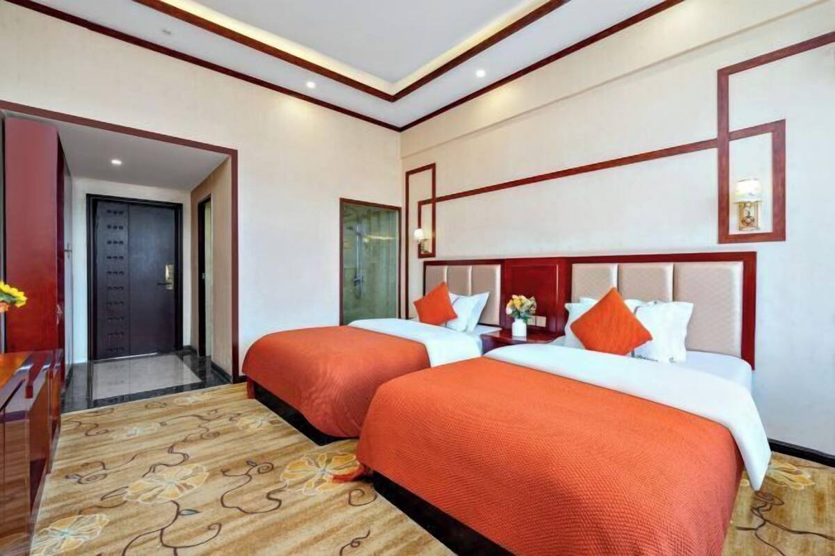 A hotel room with two beds, a wooden desk, a mirror, and a door leading to a hallway.