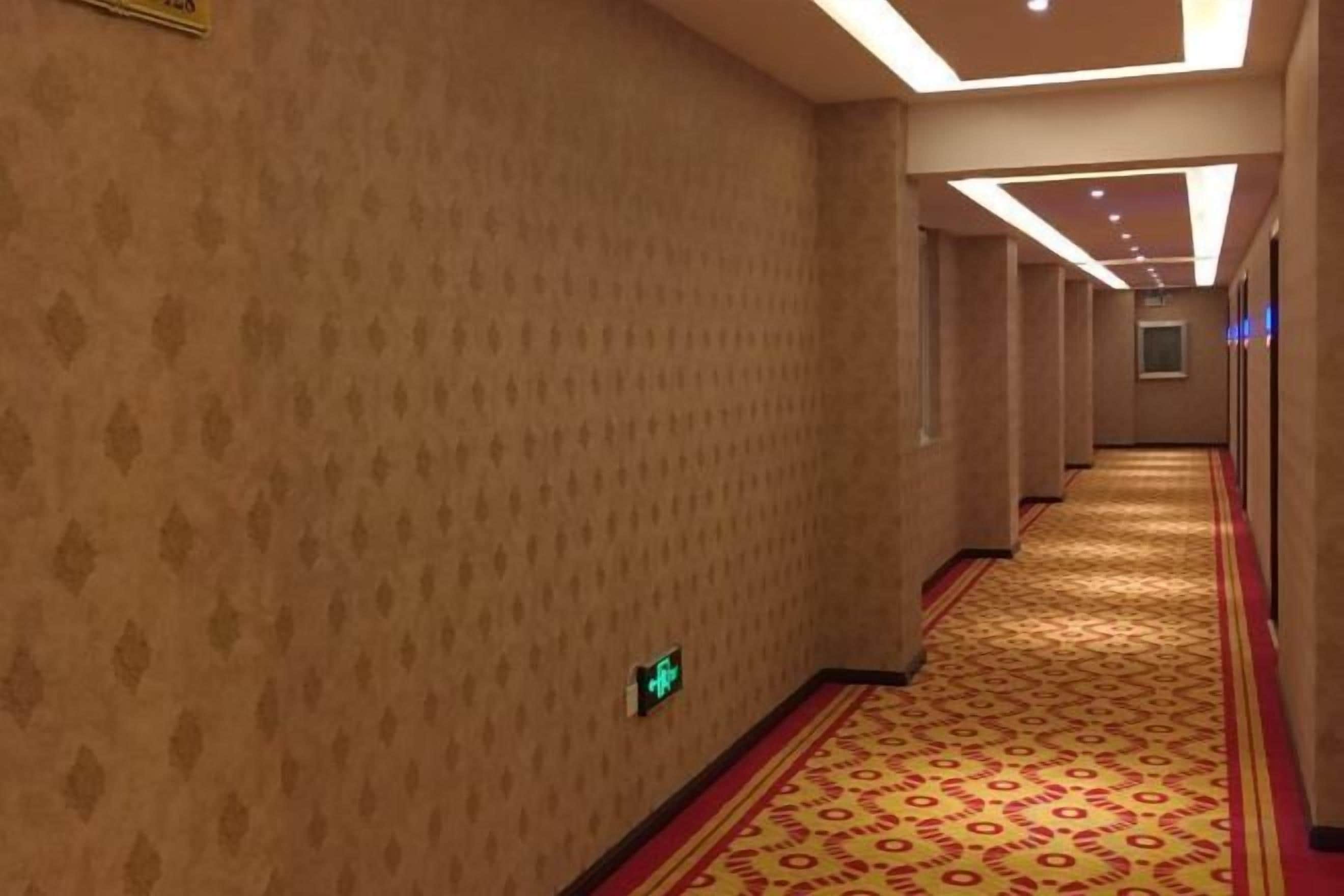Un pasillo de hotel con paredes estampadas, piso alfombrado e iluminación empotrada en el techo.