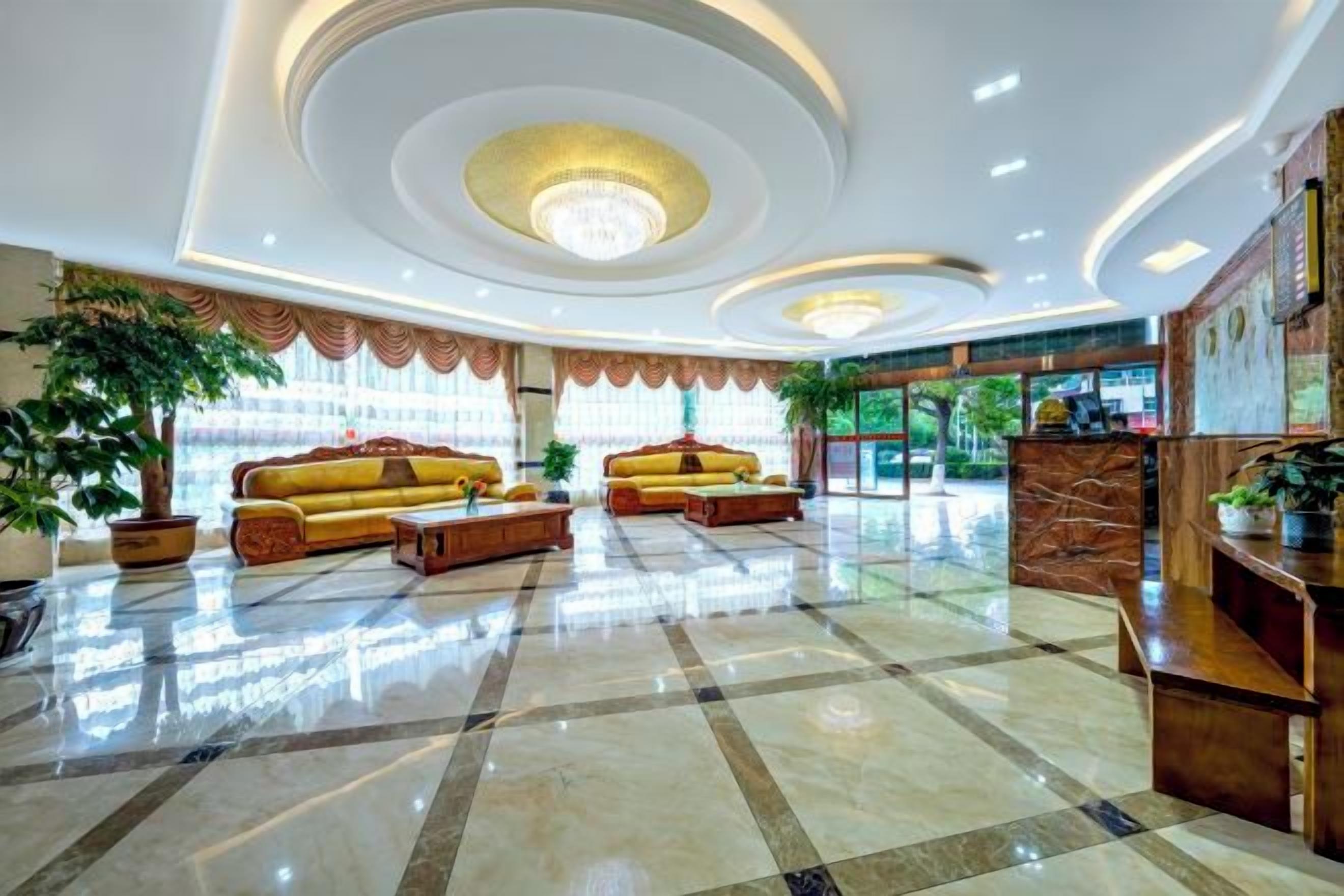A hotel lobby with a reception desk, two sofas, and a chandelier.
