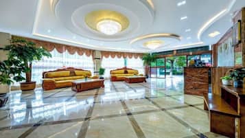 A hotel lobby with a reception desk, two sofas, and a chandelier.
