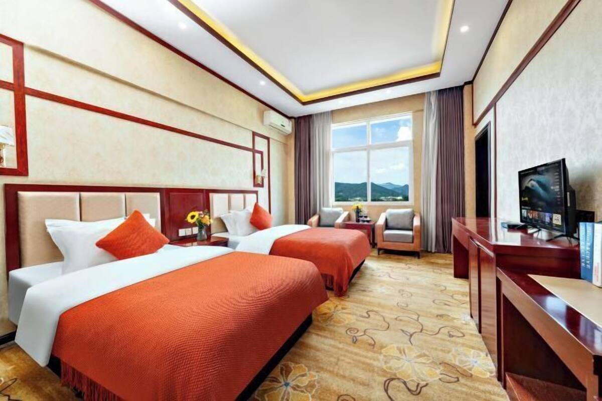A hotel room with two beds, a TV, a desk, and a view of the mountains.