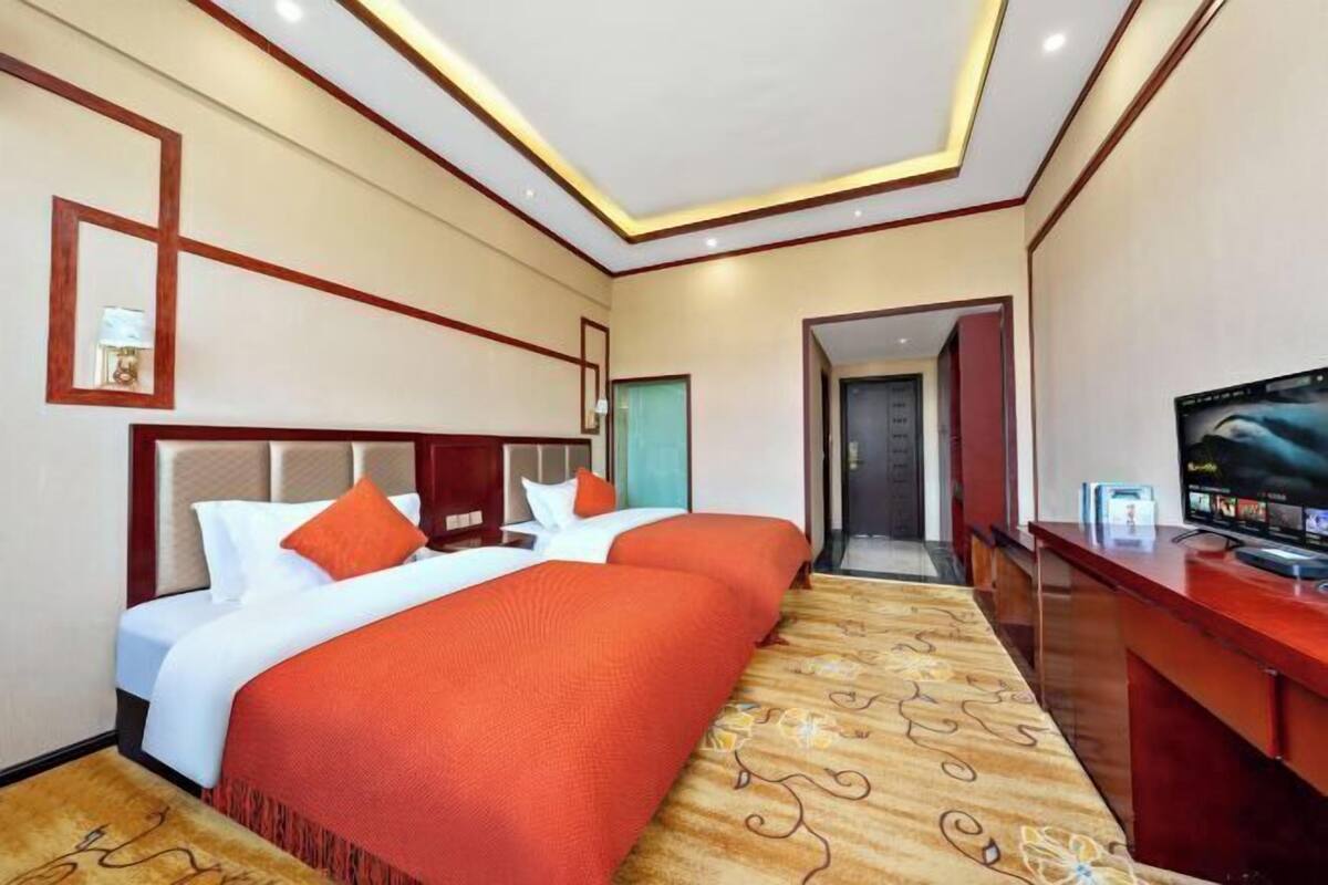 A hotel room with two beds, a TV, a desk, and a carpeted floor.