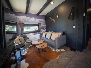 A modern living room with a grey sofa, a wooden coffee table, and a fur rug. There are windows with curtains, a radiator, and a wall-mounted light fixture. - Nice Chalet in Pressegger See With Terrace (Hermagor-Pressegger See)