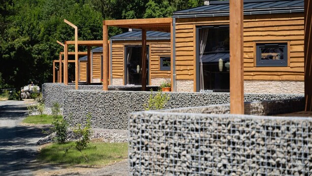 Una fila de cabañas de madera con zócalos de piedra, frente a un denso bosque.