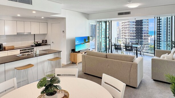 Eine moderne Wohnung mit Küche, Essbereich und Wohnzimmer. Sie verfügt über ein großes Fenster mit Blick auf die Stadt, einen Flachbildfernseher und einen Balkon.