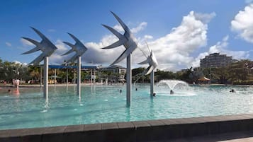 A swimming pool with large windmill sculptures, surrounded by a paved walkway and buildings in the background.