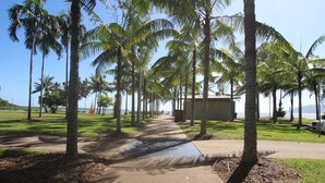 A pathway lined with palm trees leading to a building with a view of the ocean. - Unique Tropic Escape 444 (Cairns North)