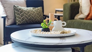 A round table with a white marble top and black metal legs, placed in a living room with a sofa and cushions in the background. - Unique Tropic Escape 444 (Cairns North)