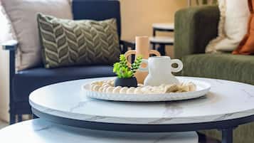 A round table with a white marble top and black metal legs, placed in a living room with a sofa and cushions in the background.